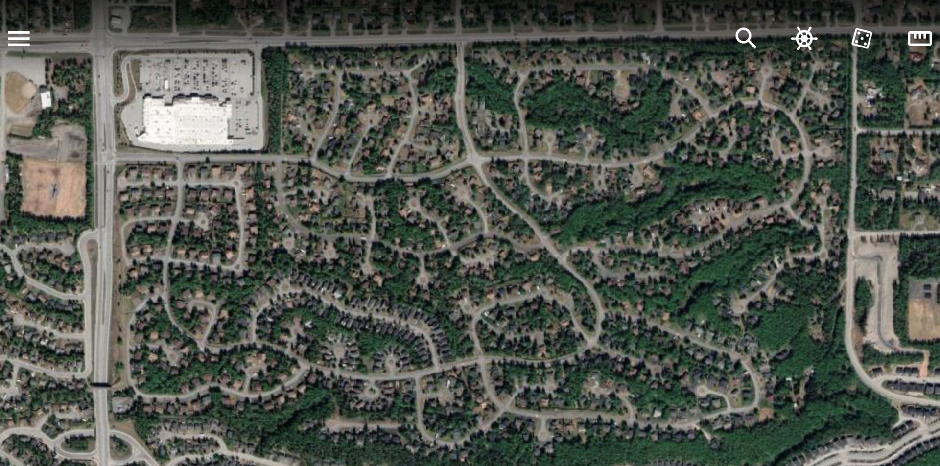 Aerial view of a residential area with winding roads, trees, and a large commercial building.