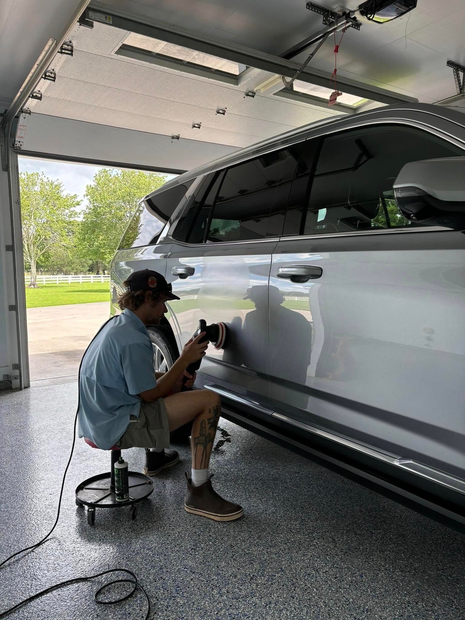 A man is polishing the side of a car in a garage.