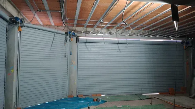 Interior de un garaje con dos puertas enrollables metálicas grises cerradas y vigas de madera a la vista en el techo.