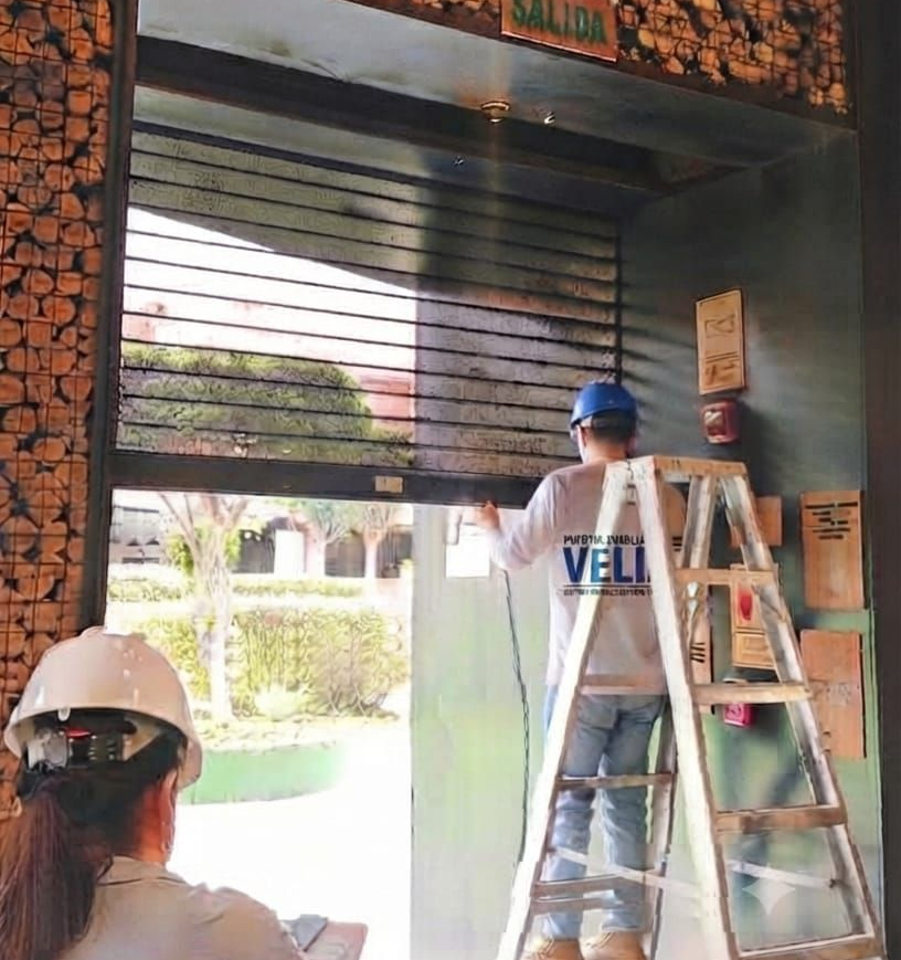 Fachada de tienda con letrero turquesa, columnas de ladrillo gris y estanterías con productos visibles en el interior.