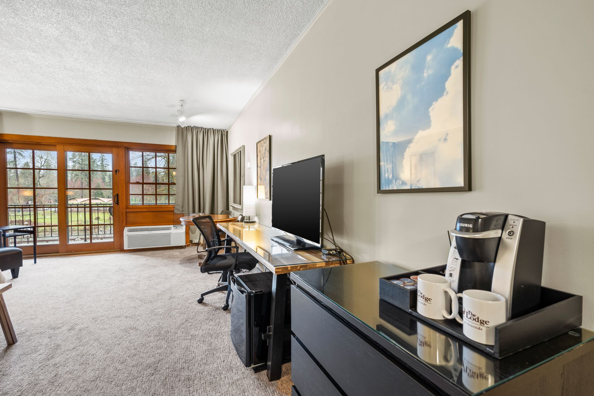 Modern living room with desk, TV, black cabinet, and large windows with balcony doors