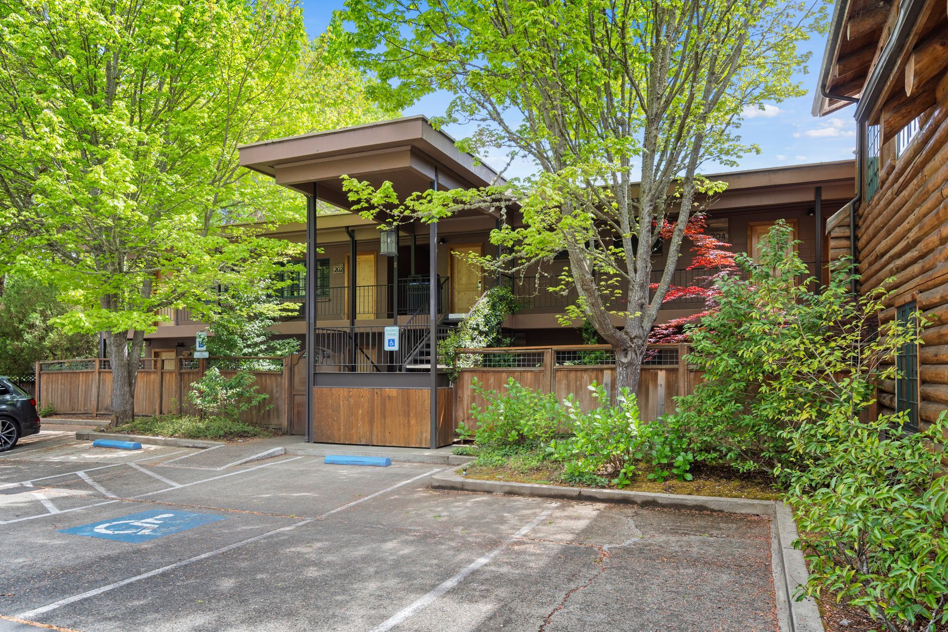 Wooded apartment entrance with wooden canopy, parking spaces, and greenery surrounding the walkway