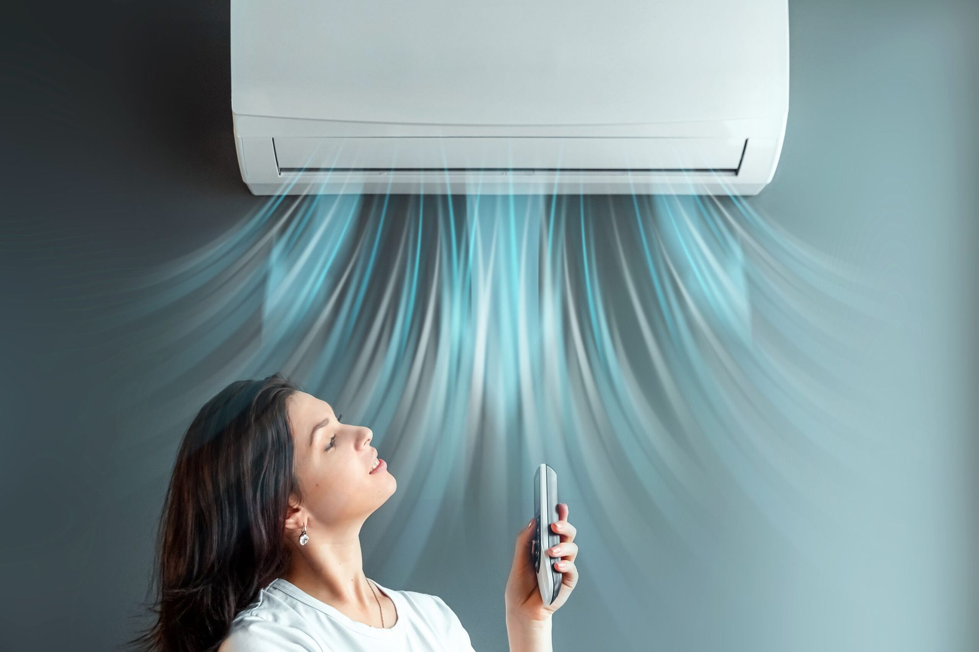 Donna che si gode l'aria fresca proveniente da un condizionatore a parete, tenendo in mano il telecomando, in casa.