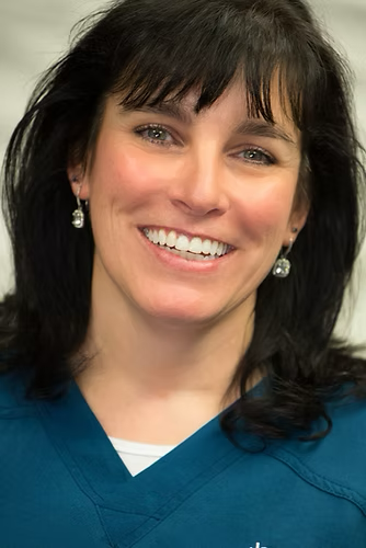 Woman with dark hair smiling, wearing a teal top and silver earrings.