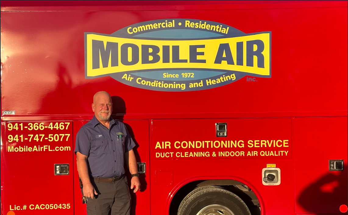 Man in blue uniform stands by red Mobile Air truck; offers air conditioning services.
