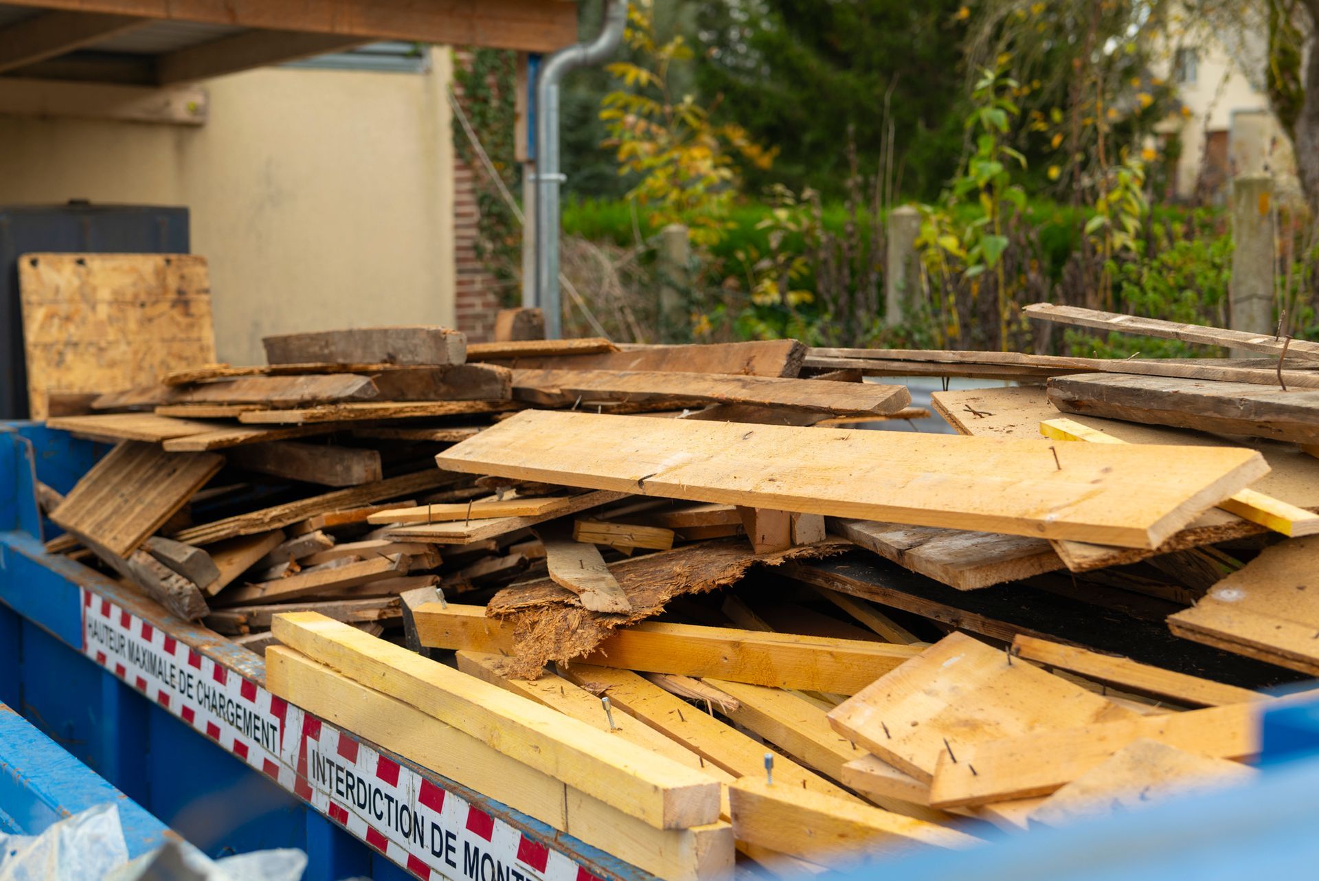 Débris de bois, notamment des planches et des madriers, dans un conteneur bleu à l'extérieur.