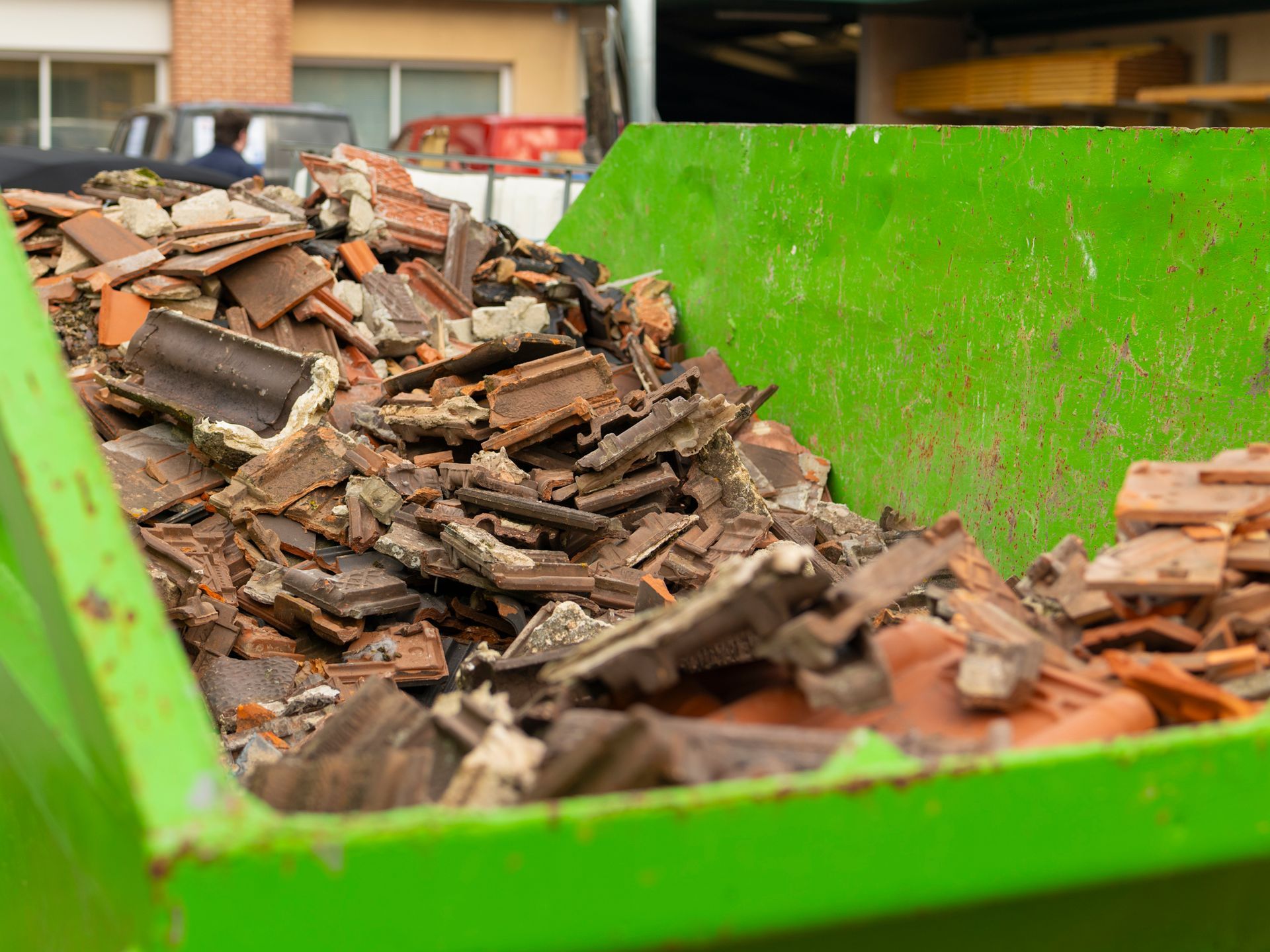 Conteneur à déchets vert rempli de tuiles cassées.