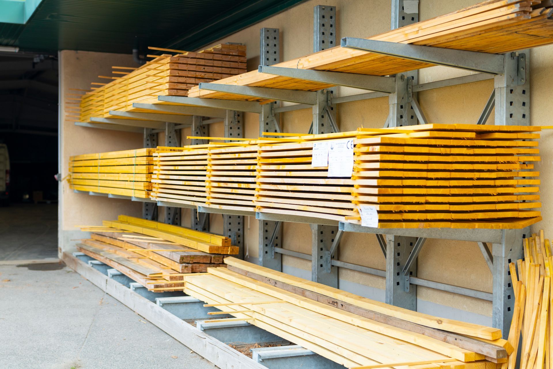 Planches de bois stockées sur des étagères industrielles en porte-à-faux contre un mur beige.