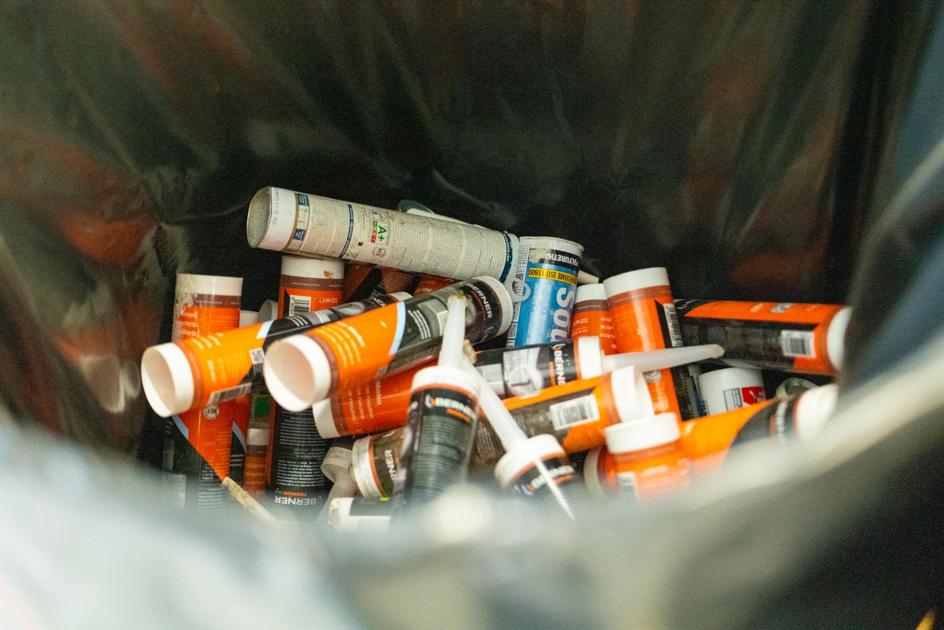 Poubelle remplie de tubes de mastic orange et blanc.