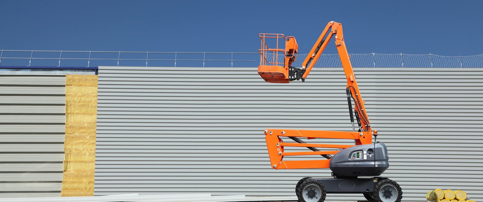 Un ascenseur orange est déployé vers un mur en tôle ondulée grise.