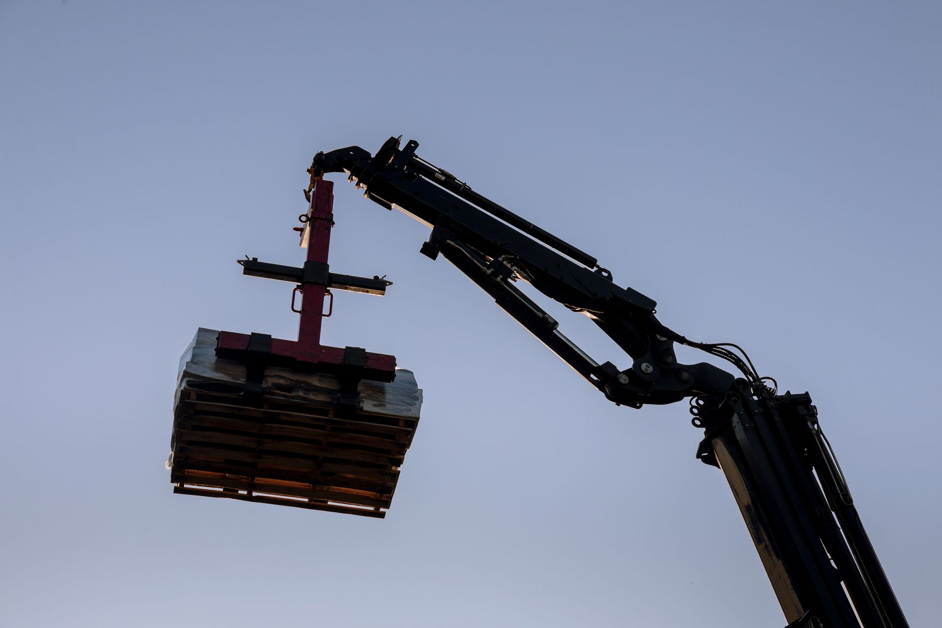 Une grue hydraulique soulève une charge rectangulaire sur fond de ciel crépusculaire.