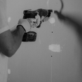A person in gloves uses a drywall screw gun to fasten a screw into a white wall.