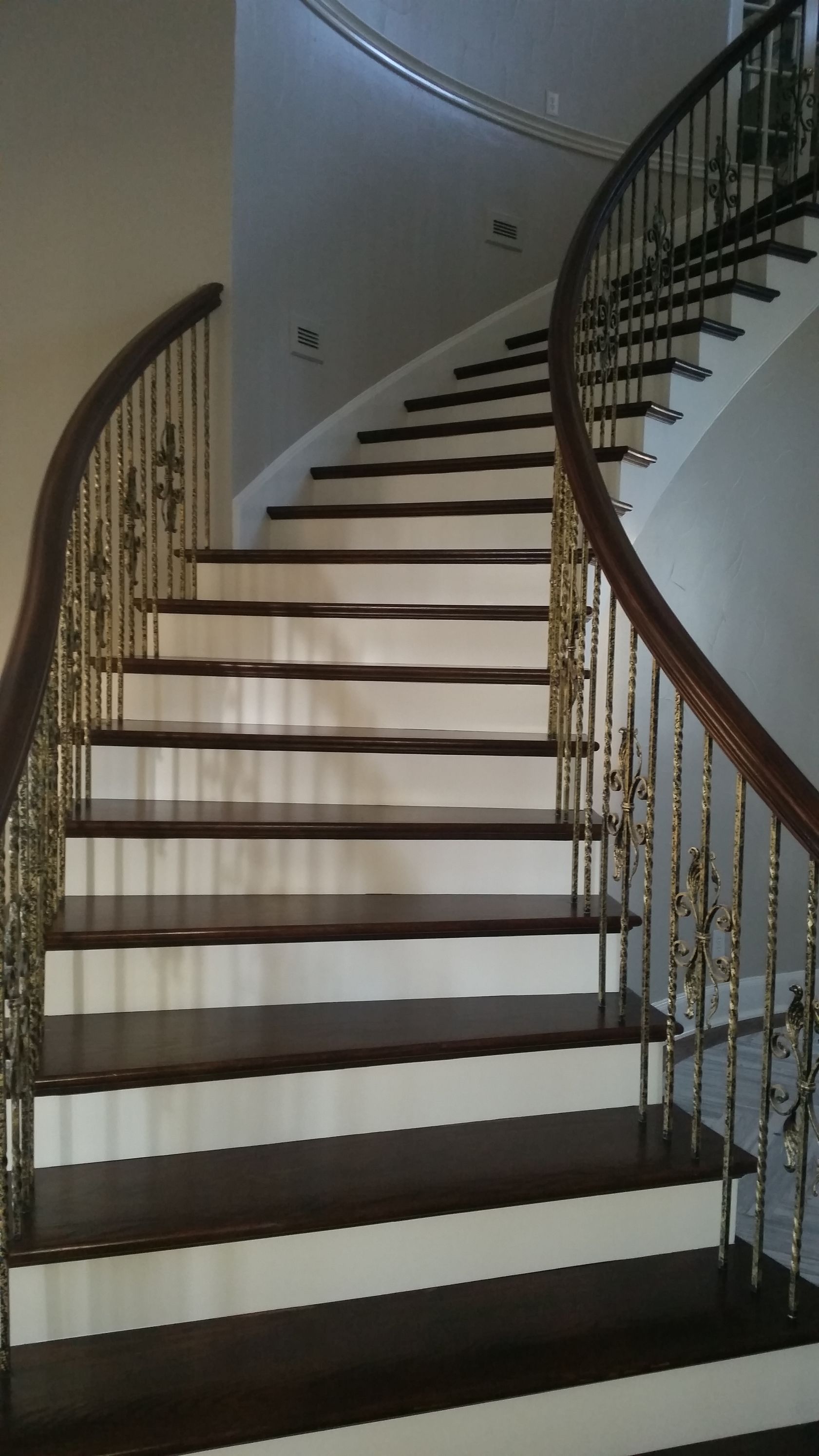 Curved indoor staircase with white steps, dark wooden treads, and wrought-iron railing.
