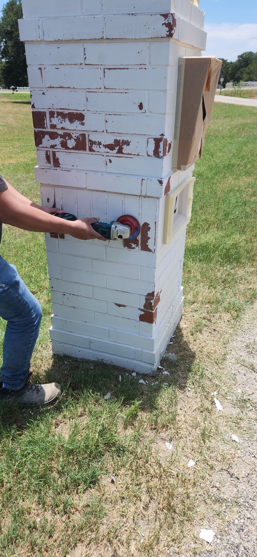 Person painting a white brick column outdoors with a paint roller