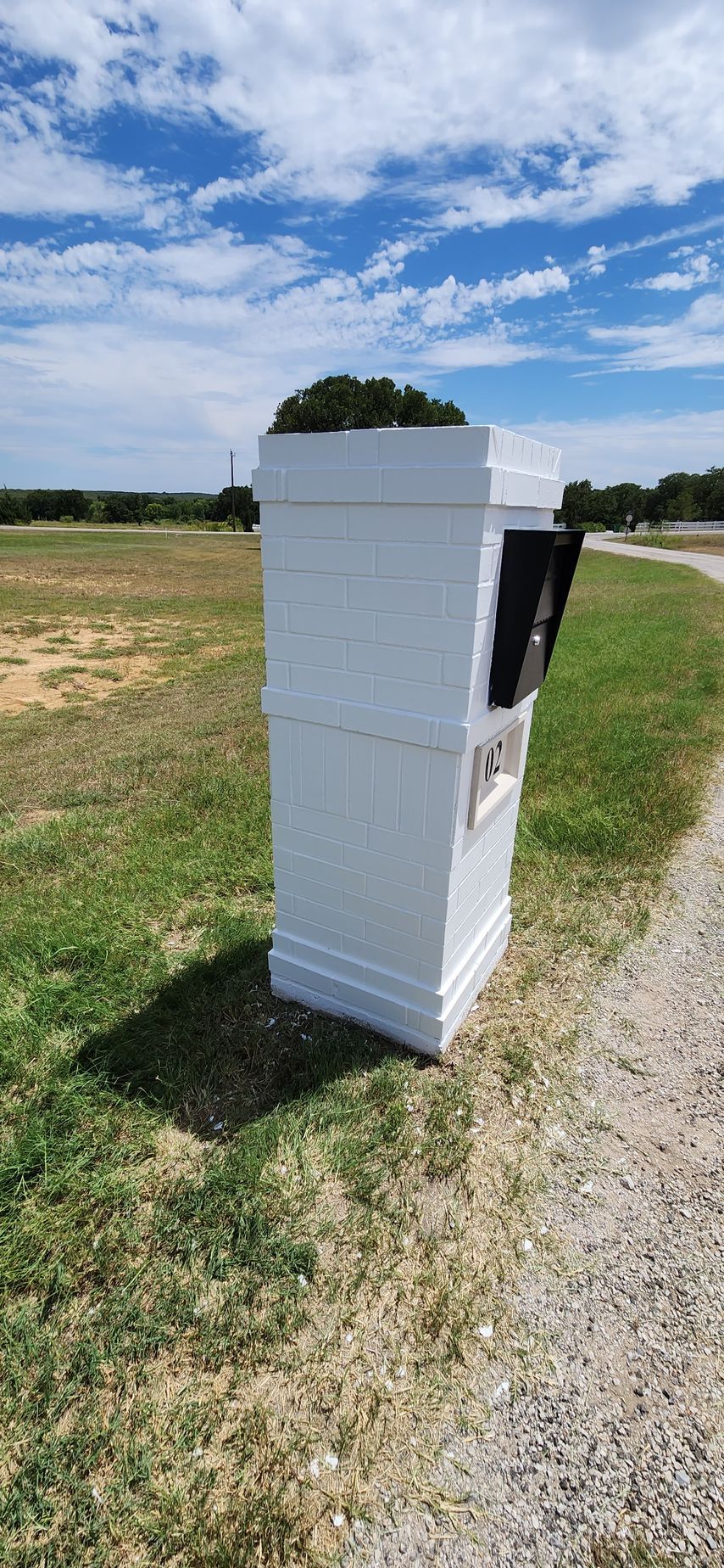 White roadside utility box on a grassy field under a blue sky with clouds