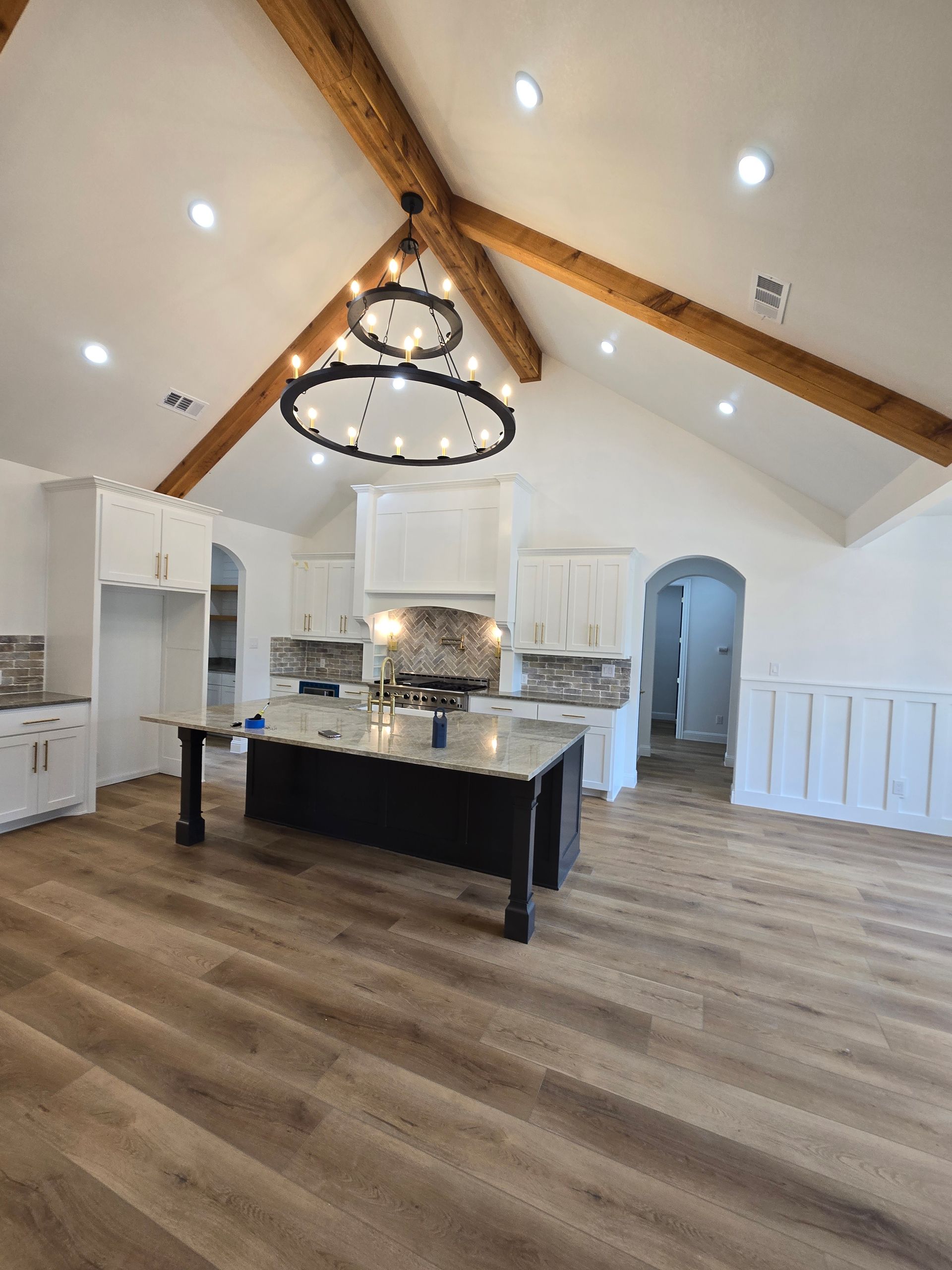 Bright modern kitchen with island, white cabinets, wood beams, and chandelier under vaulted ceiling