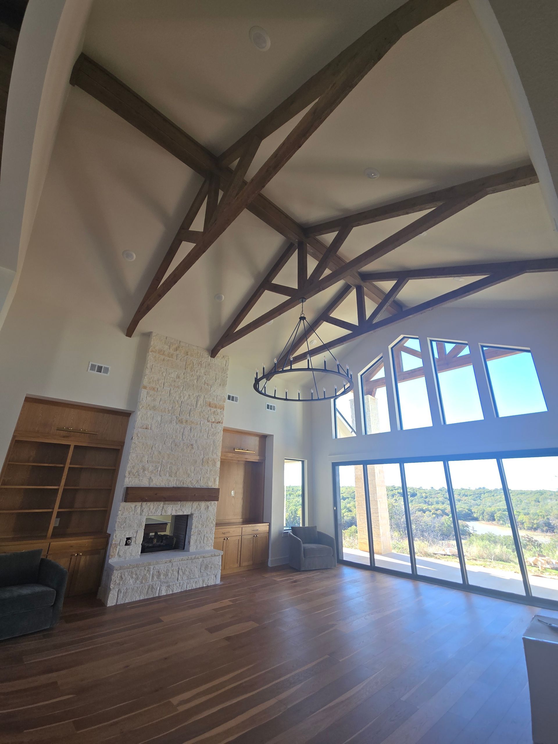 Spacious modern living room with exposed wood beams, fireplace, hardwood floors, and large windows overlooking a view.