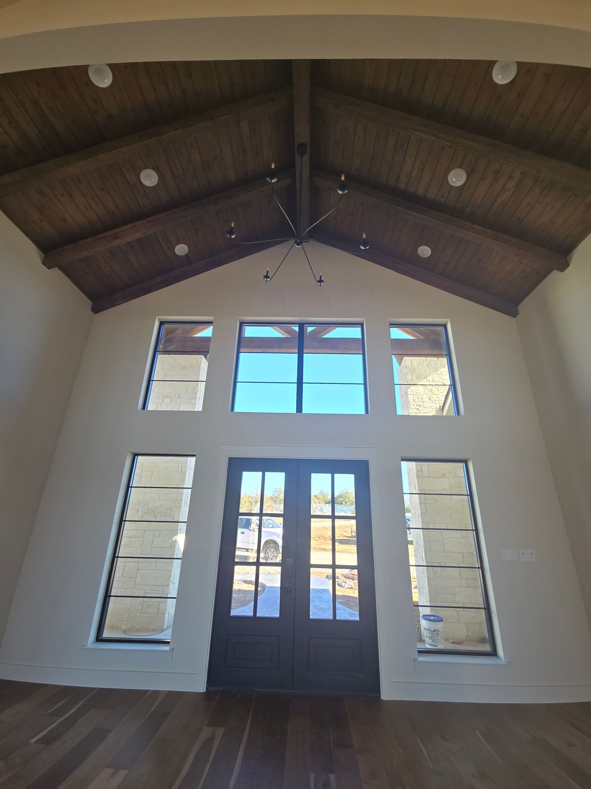 Interior of a church or hall with tall white walls, wooden vaulted ceiling, and large double doors centered below windows.