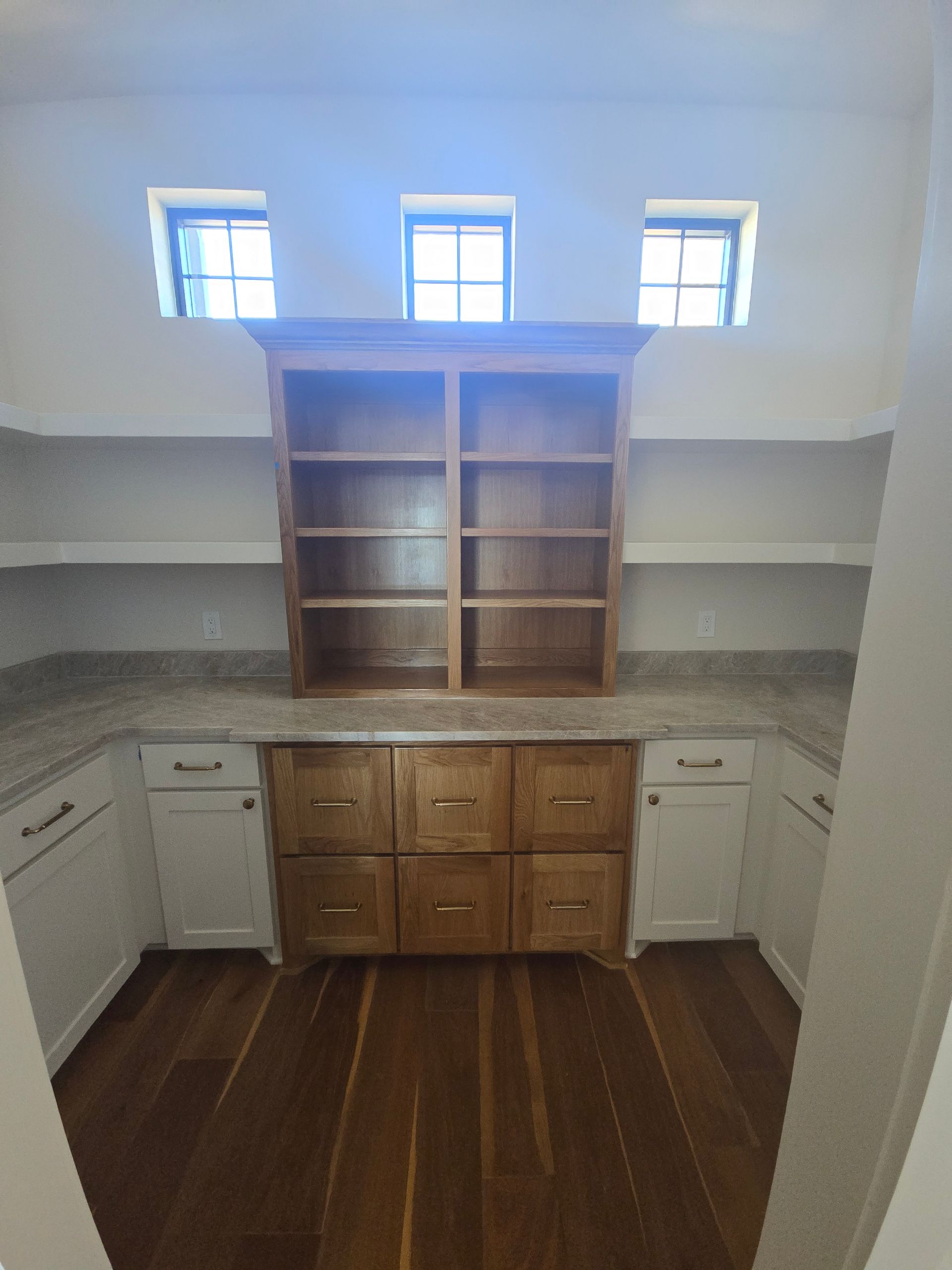 Built-in pantry nook with wooden cabinets, open shelves, marble counters, and small windows above.