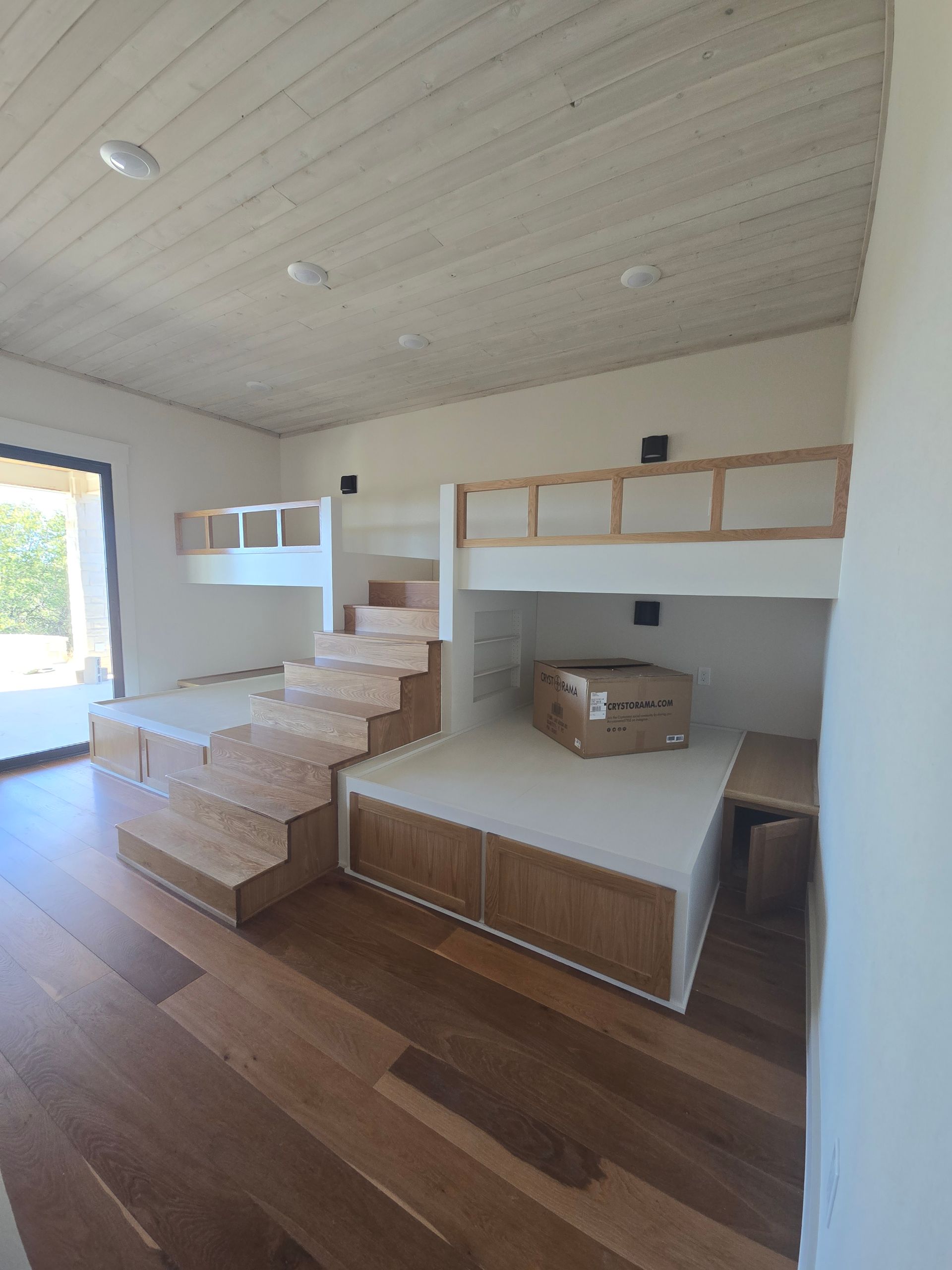 Modern loft-style room with wood floor, built-in bunk beds, and a central staircase to an upper sleeping area