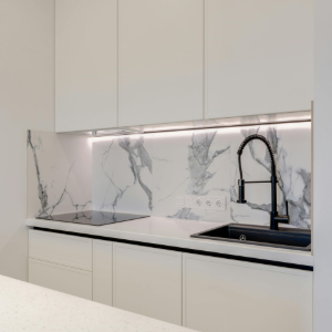 Modern kitchen featuring white flat-panel cabinets, marble backsplash with LED lighting, and a black sink and faucet.