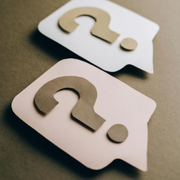 Two speech bubbles with question marks, one white and one light pink, arranged against a dark brown background.