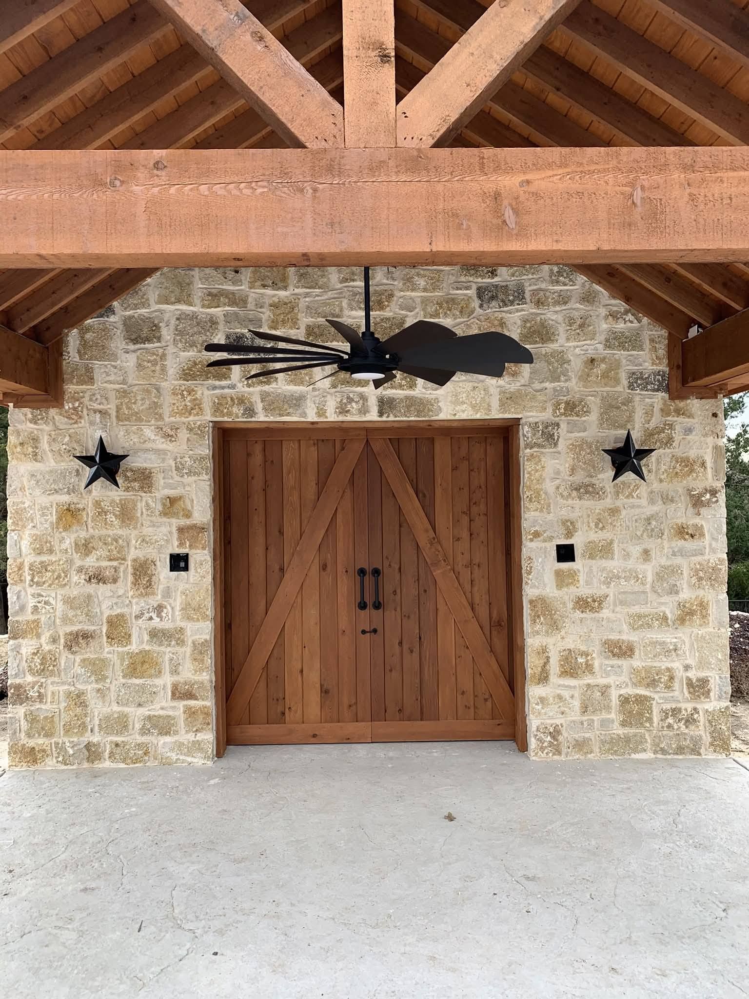 Covered stone entryway with rustic wooden double doors, exposed timber beams, and ceiling fan