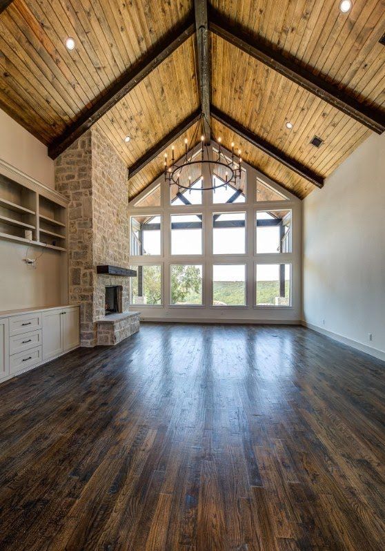 Bright vaulted living room with wood ceiling, large windows, dark floors, and built-in shelves