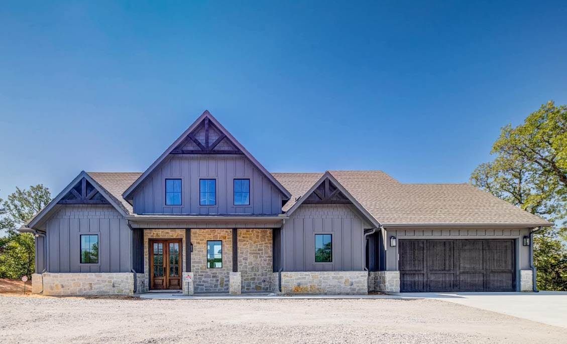 Modern gray house with stone accents, three garage doors, and a clear blue sky