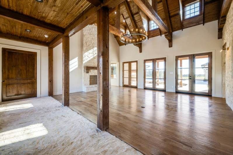 Spacious rustic room with wood beams, hardwood floors, and large windows letting in natural light