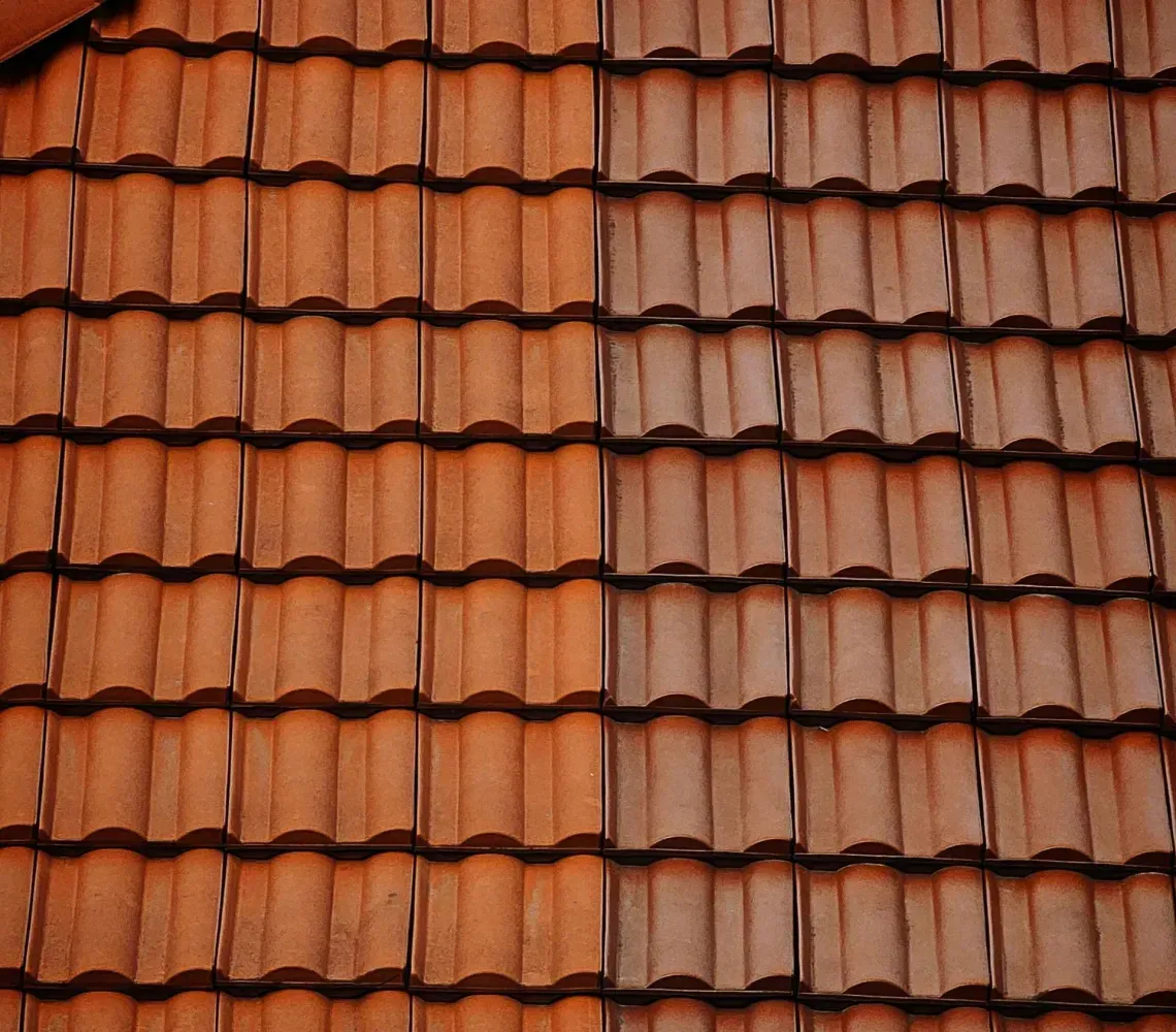 A split-view of a tiled roof, showing the left side cleaned and bright orange, contrasting with the dirty, gray right side.