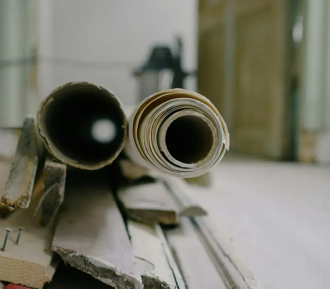 Two paper rolls rest on a pile of wooden planks and a red cord, with a blurred doorway in the background.