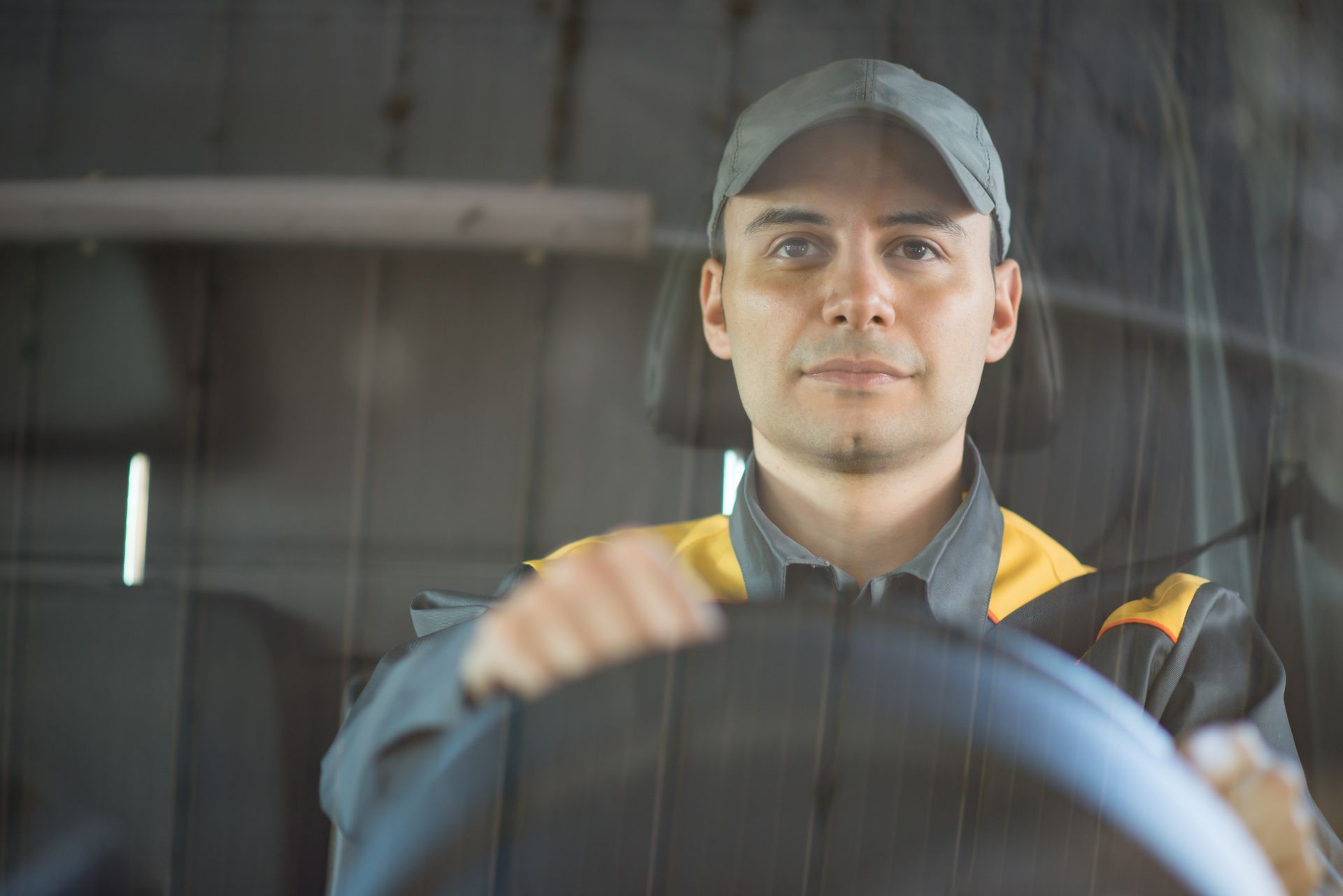 Person in a cap driving a vehicle, seen from the front through the windshield.