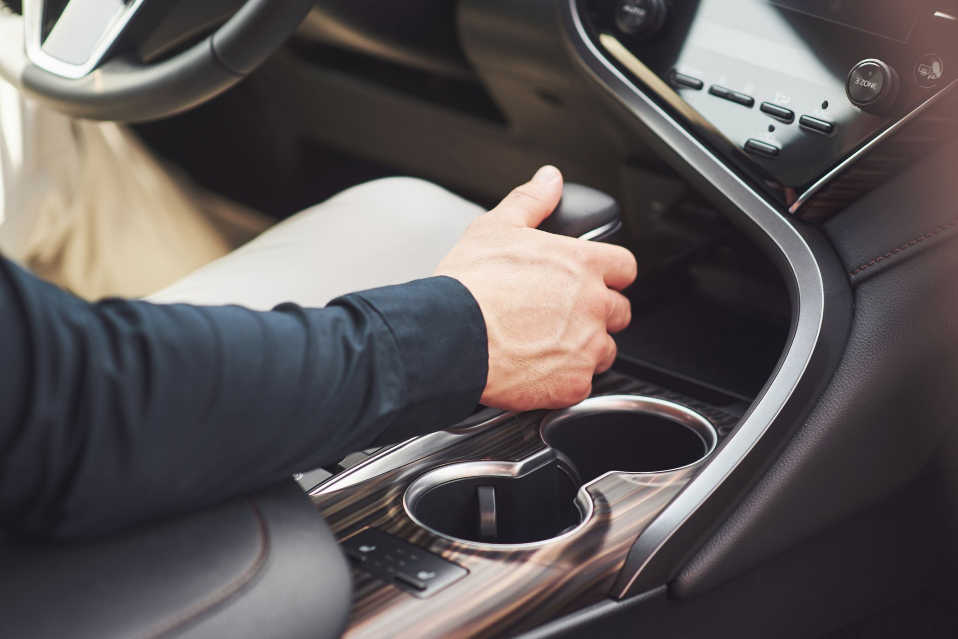 Hand adjusting a car’s center console near the cup holders and gear selector