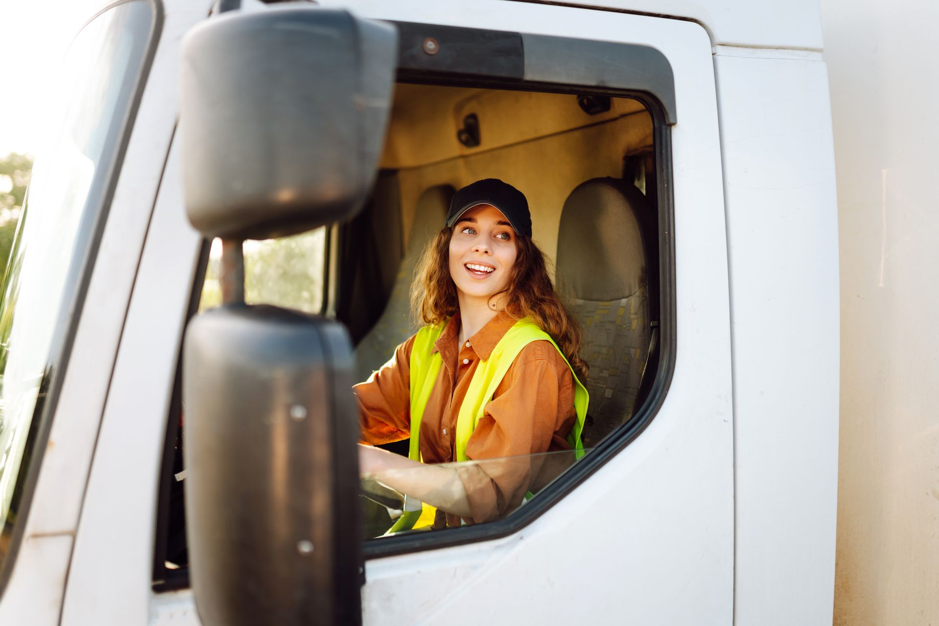 Truck driver smiling in the cab, wearing a reflective safety vest and hard hat