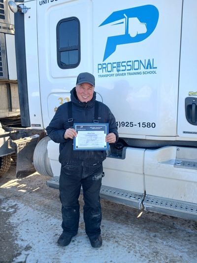 Person in dark workwear holding a certificate in front of a white and blue truck trailer.