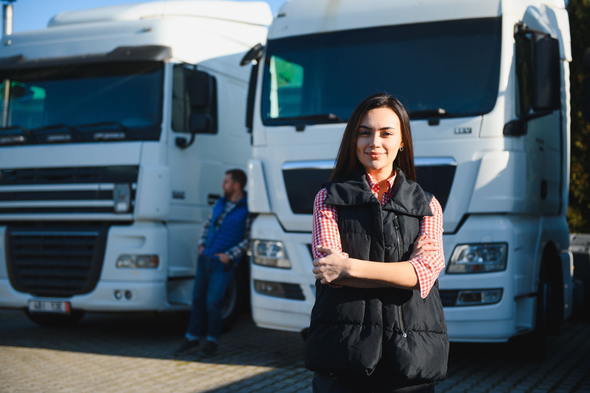 Woman standing with arms crossed in front of white trucks at a loading area.