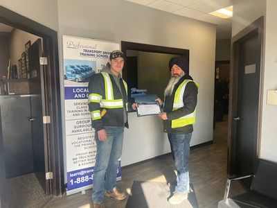 Two workers in safety vests holding a certificate inside an office lobby