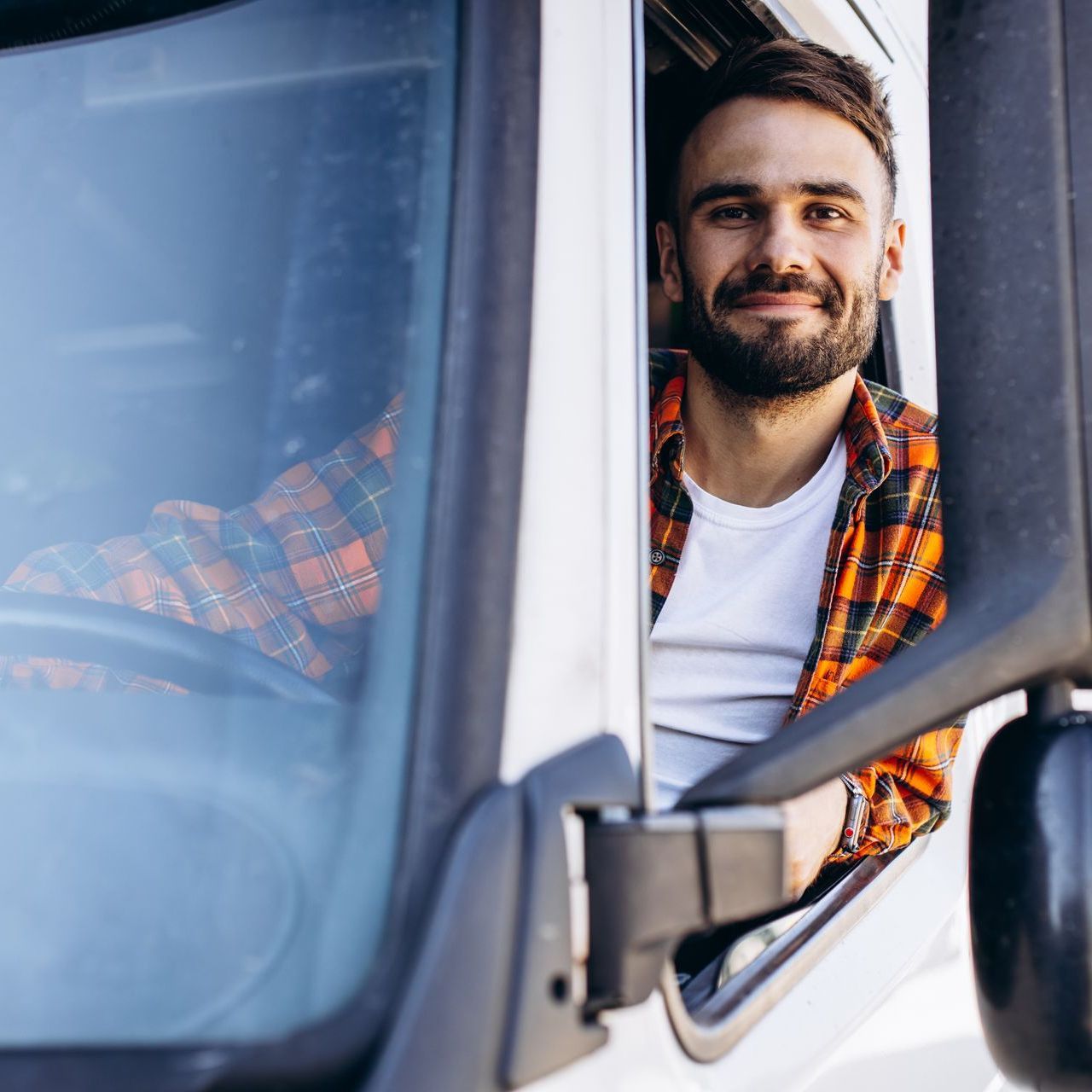 a man in a plaid shirt is sitting in the driver 's seat of a truck .