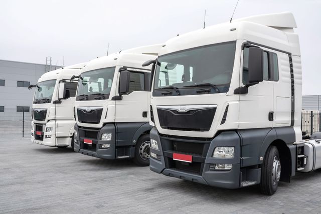 a row of white semi trucks parked next to each other in a parking lot .