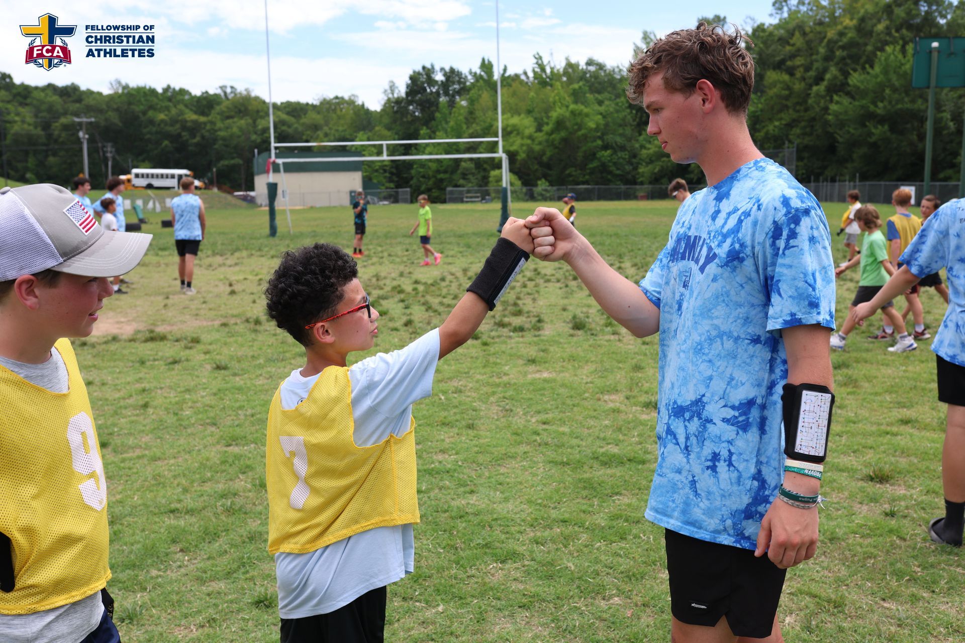 A young athlete in a yellow jersey exchanges a fist bump with a participant in a blue shirt on a sports field.
