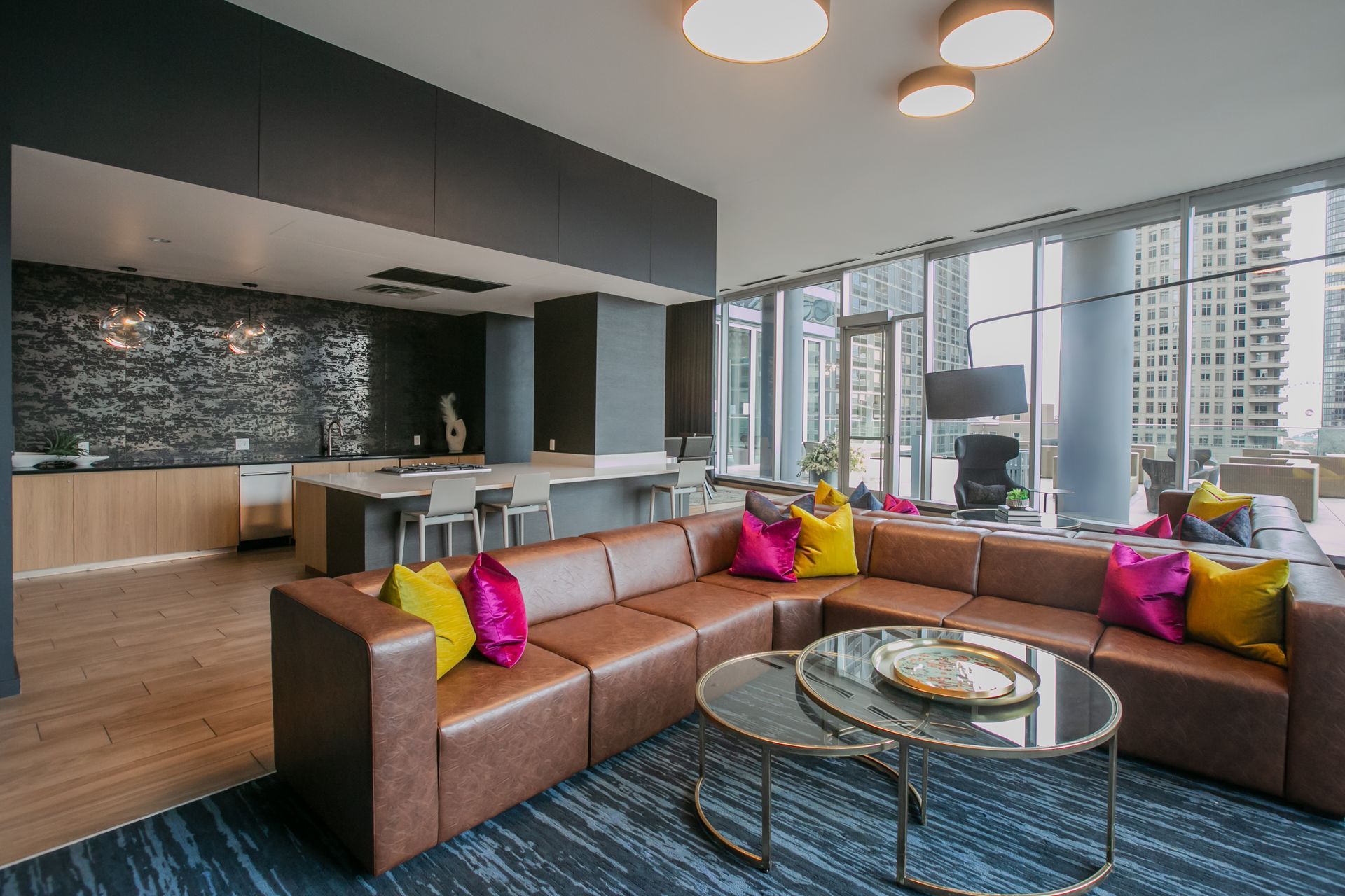 Lounge area with blue sectional sofa, two armchairs, round coffee tables, and neutral patterned rug.