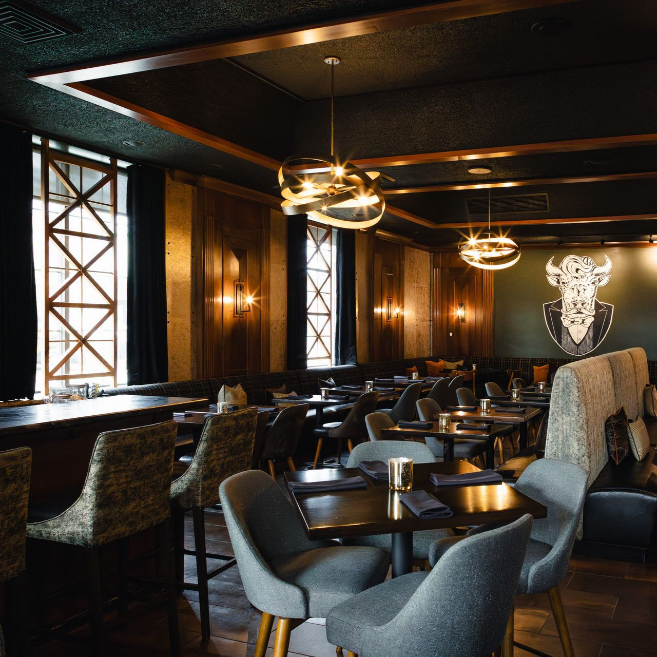 Elegant restaurant interior with tables, chairs, and lighting fixtures. Dark wood paneling and decorative wall art.