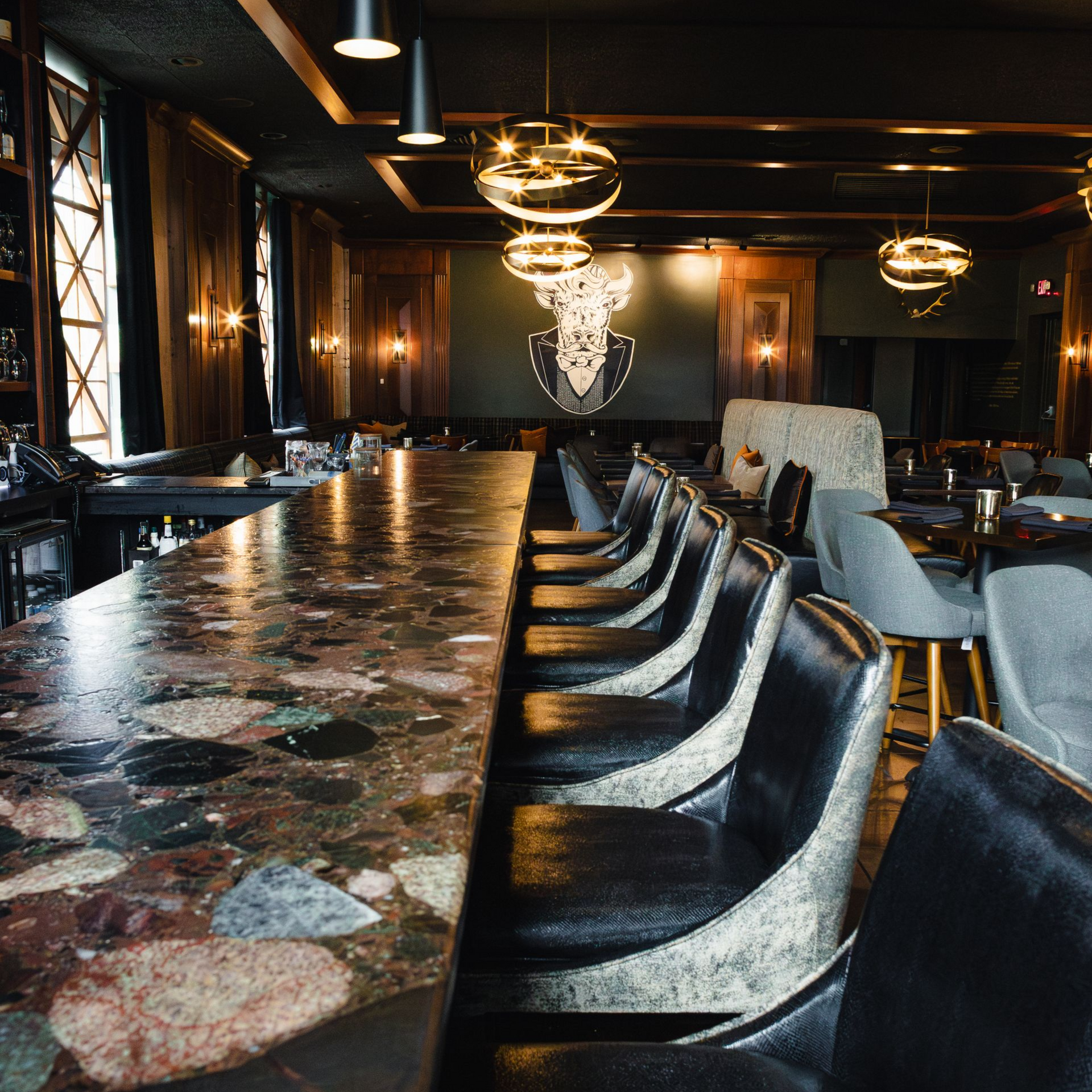 Dark bar with a long stone countertop, leather bar stools, and decorative pendant lights.