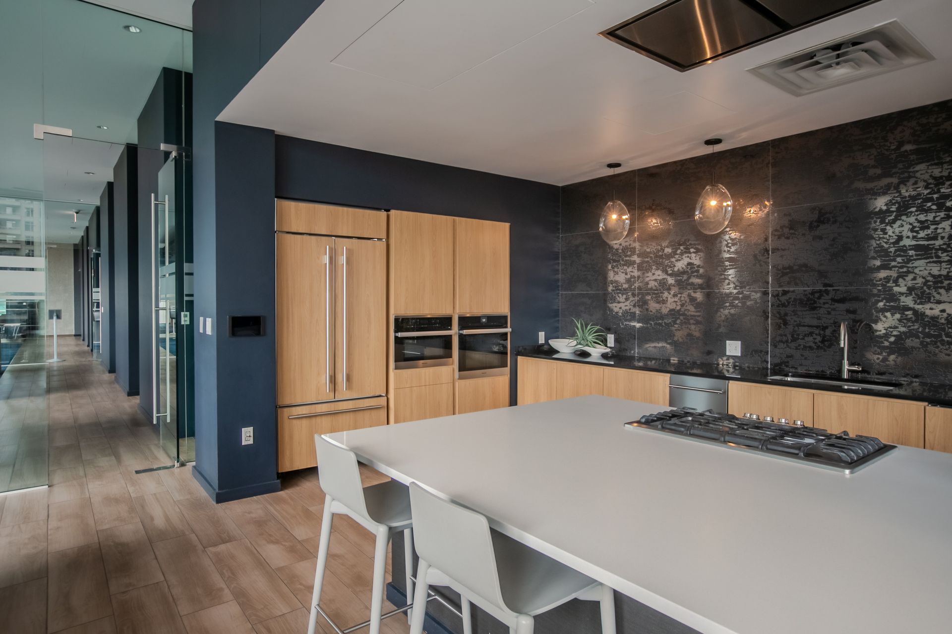 Modern kitchen with light wood cabinets, dark backsplash, island with stools, and wooden floor.
