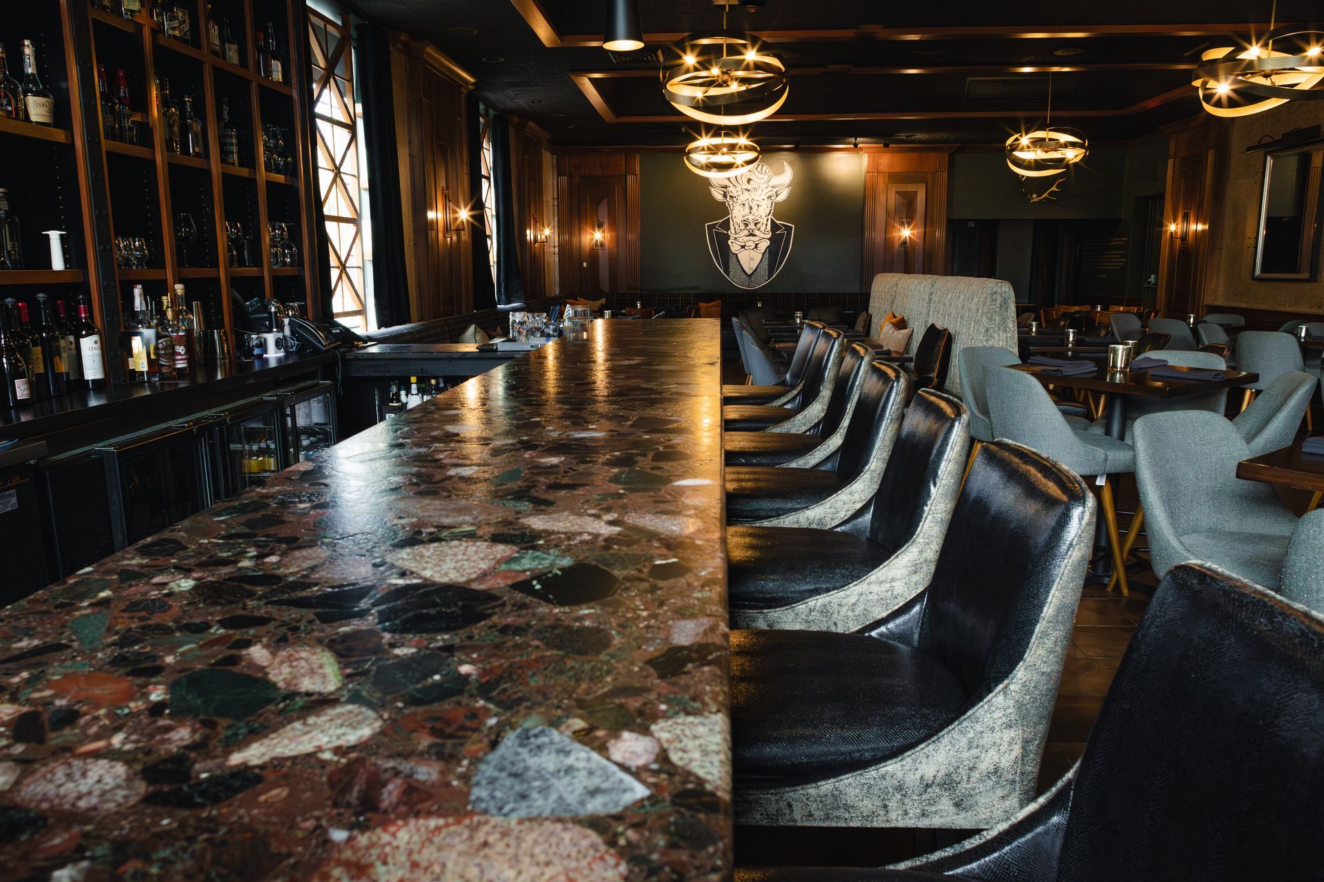 Bar interior with long patterned counter, dark chairs, and gold lighting fixtures.
