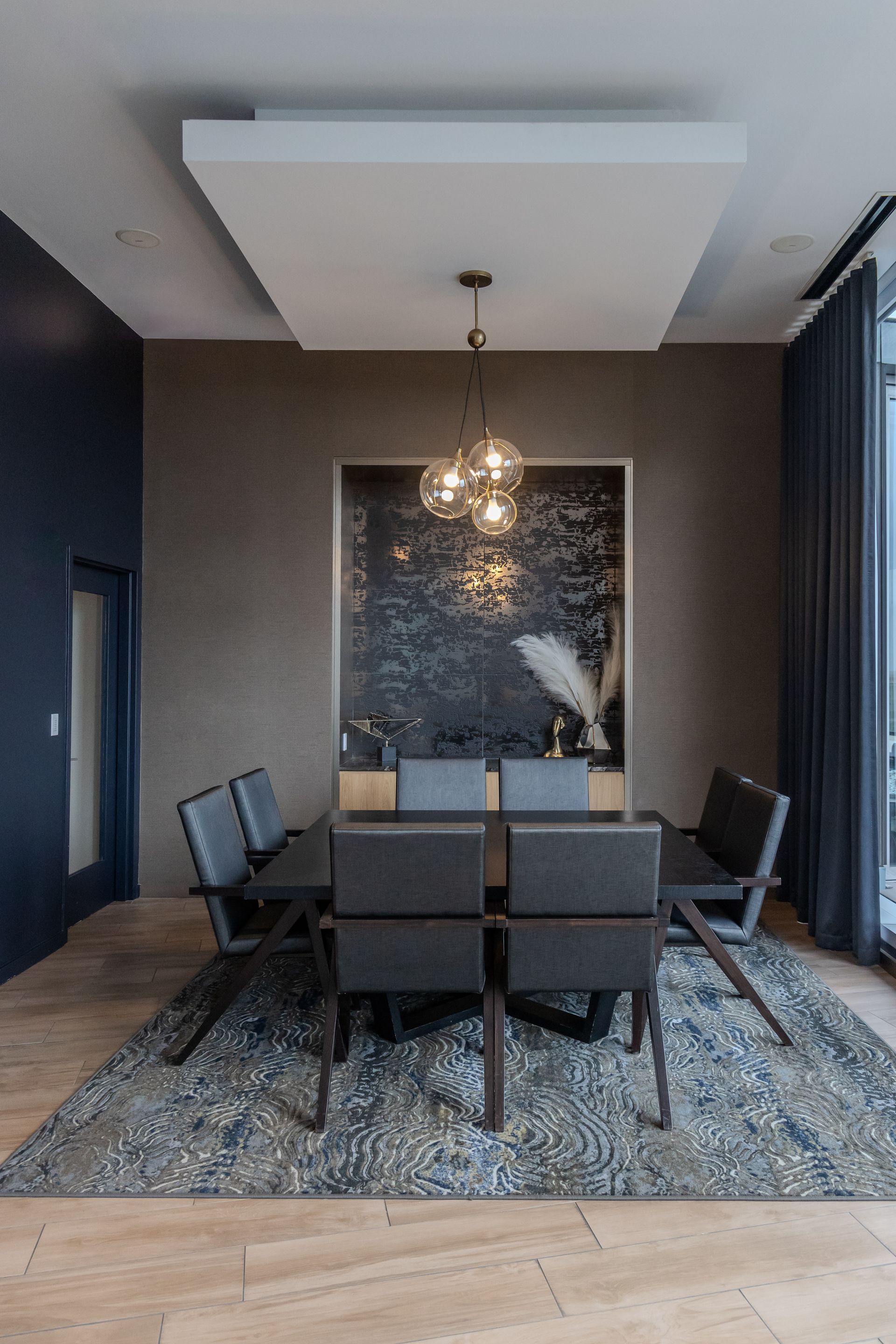 Dining room with dark furniture, blue rug, abstract art, and a light fixture.