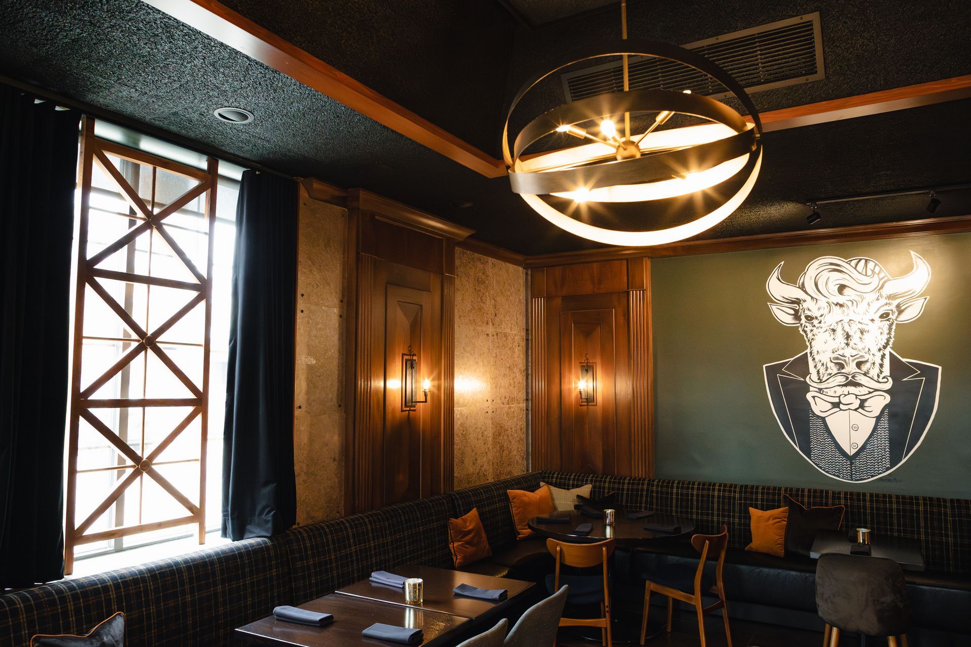 Dark restaurant booth with a bull graphic, golden chandelier, and window with sunlight.