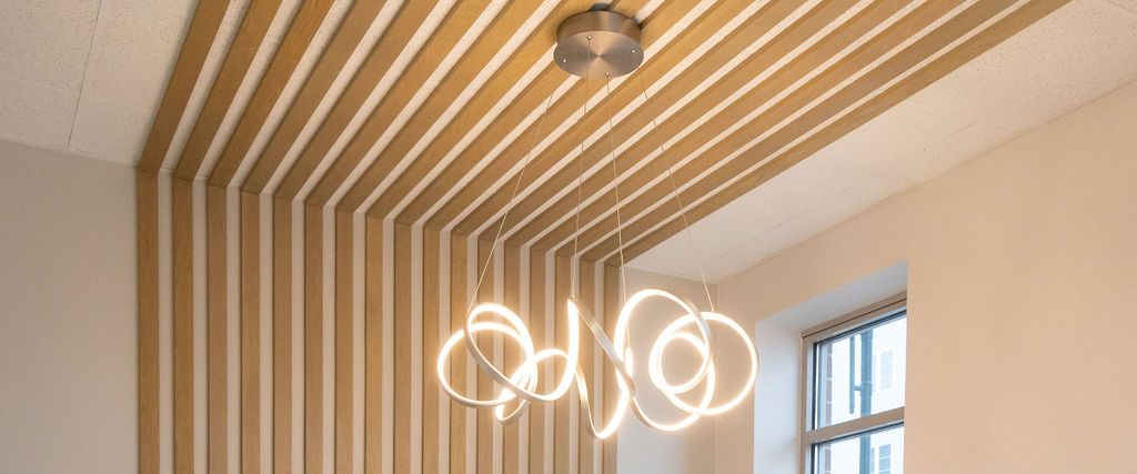 Modern room ceiling with wood slats, sculptural ring chandelier, and a window