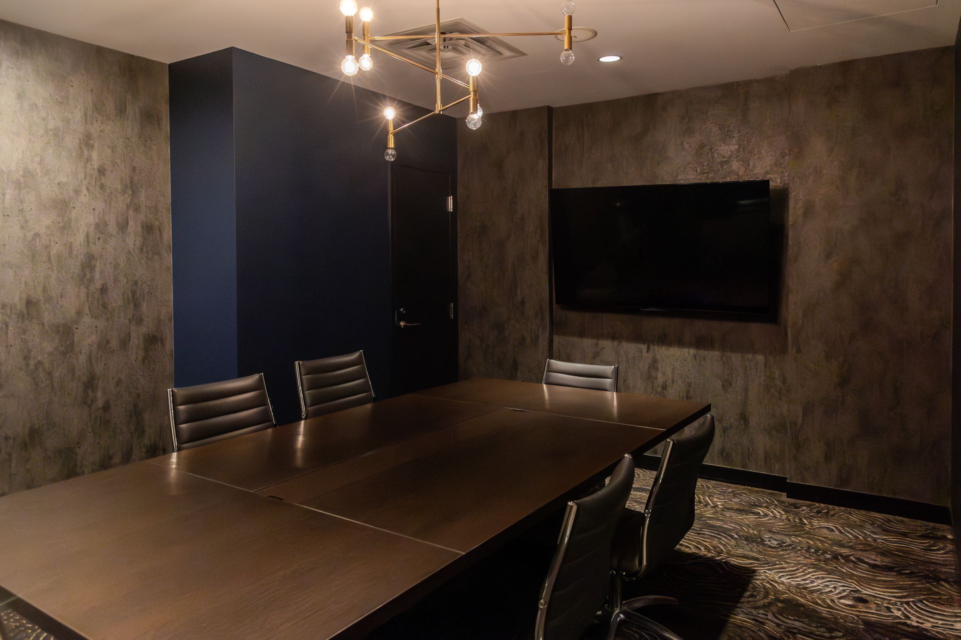 Conference room with dark wood table, chairs, TV, textured wallpaper, and chandelier.
